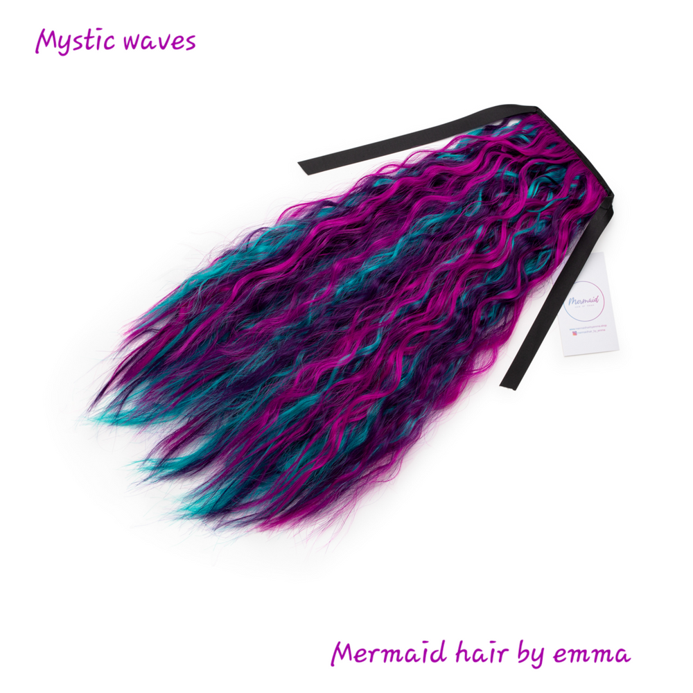 A clip-in mermaid hair extension with wavy textured hair in multiple colors, predominantly purple and black, with a ribbon attached.
