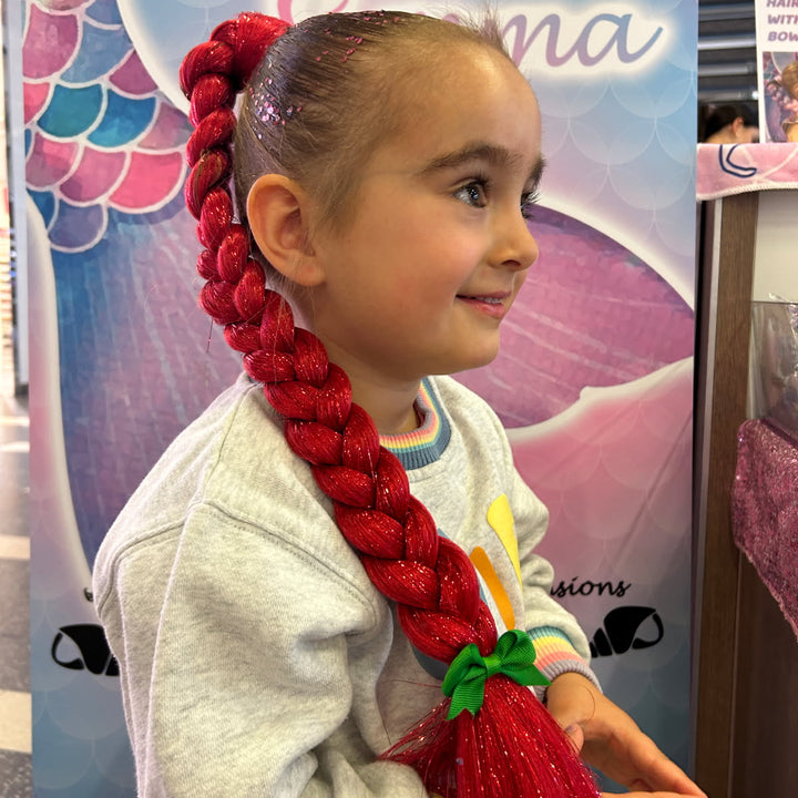 Child with red braided hair in front of a 'Hair by Emma' sign