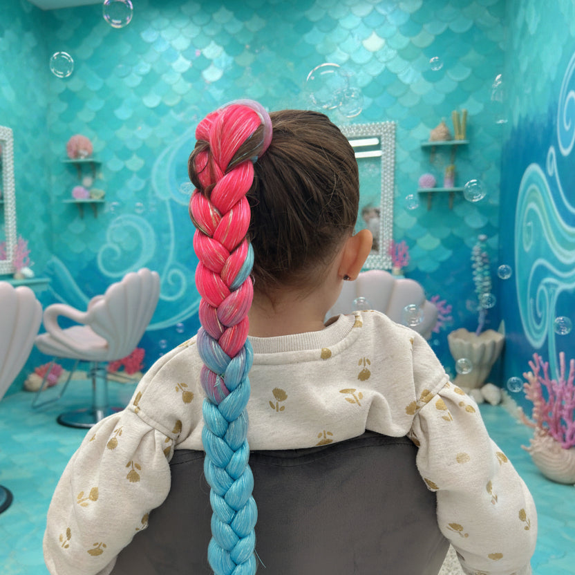 Child with colorful braided hair sitting in a chair, with a mermaid background