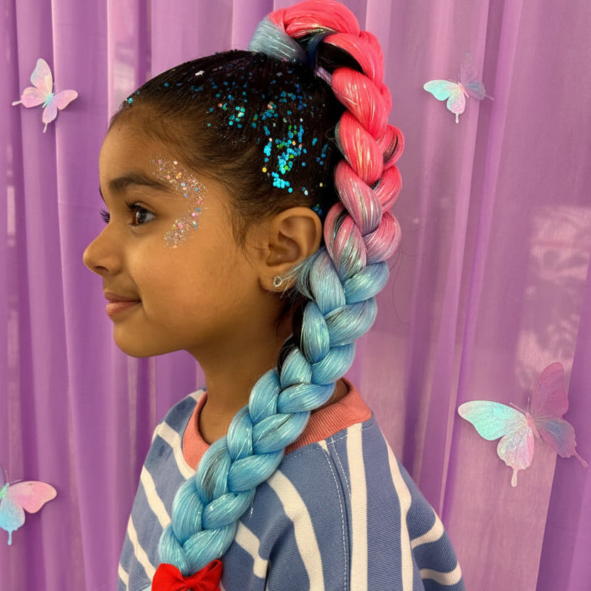 Child with colorful braided hair in front of a purple curtain