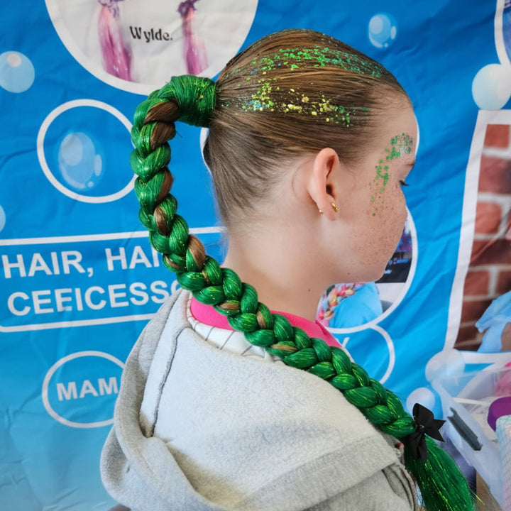 Child with green braided hair in front of a colorful background