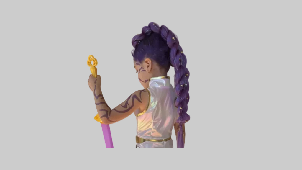 Child with purple hair in braids, body paint, and a colorful outfit holding a toy against a brick wall.