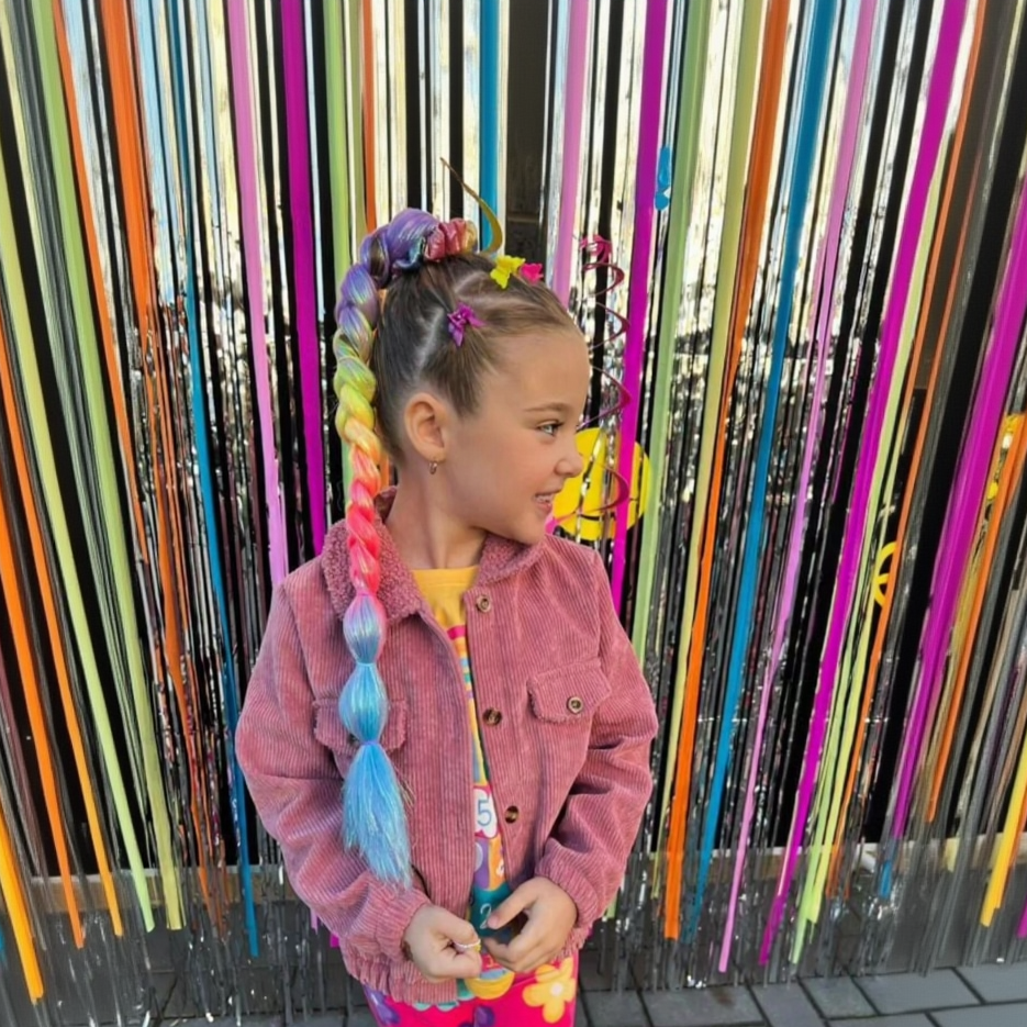 Child with colorful braids standing in front of a vibrant, striped background