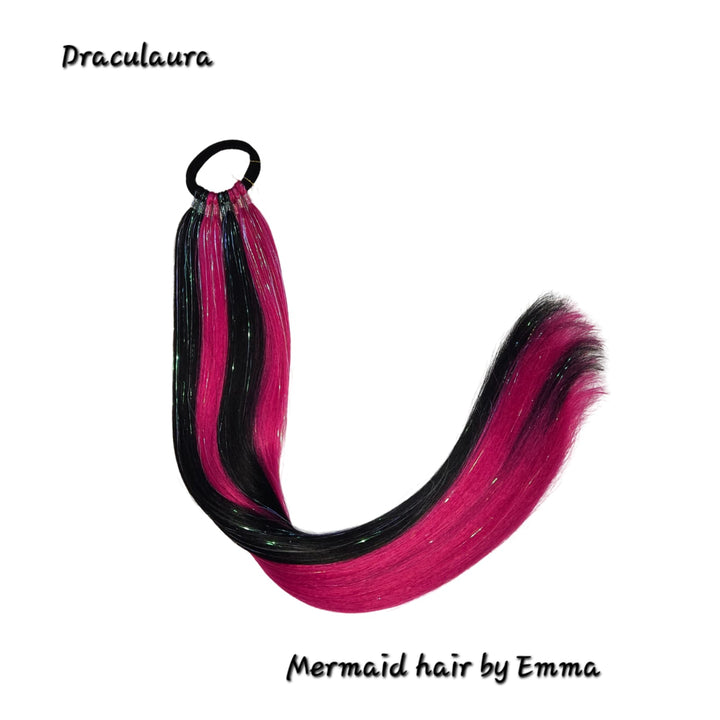 A child's synthetic hair extension styled in a mermaid tail shape with black and purple strands, labelled with 'Draculaura' and 'Mermaid hair by Emma'.