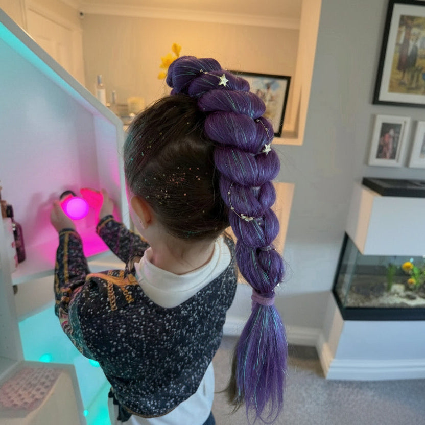 Child with a large purple braided ponytail in a room with a colorful light.