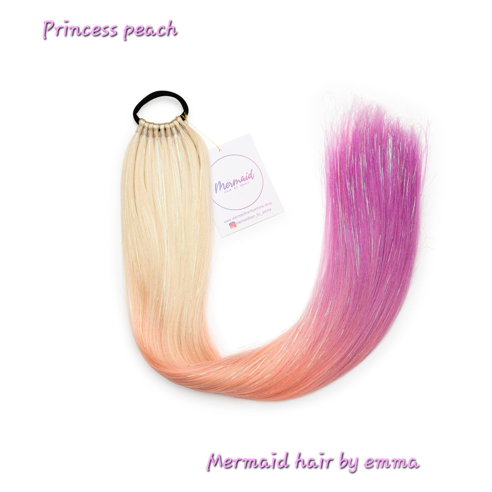 A set of reusable tie-in hair extensions for kids with a gradient of peach to pink color, labeled 'Princess Peach' by Mermaid Hair by Emma.