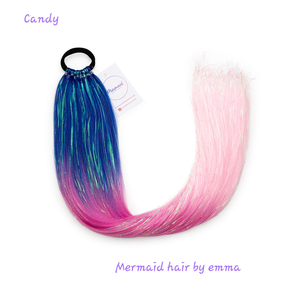 A child's synthetic hair extension with blue and pink colors, tied into a long braid with an elastic band at the top, labeled with the brand 'Mermaid hair by emma' and the name 'Candy'.